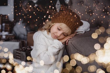 Noel ağacının yanında örülmüş şapkalı bir kız yeni yıl dileği diliyor. Noel arifesinde heyecanlı küçük kız. Umut Noel Baba 'yı bekliyor. Umutlu çocuk. Yeni yıl arifesi. Hayaller gerçek olur..