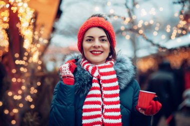 Noel pazarında punç içen genç bir kadın. Caddede dikilmiş sıcak şarap, çay ya da kakao içen, kışın açık havada sıcak kahve içen güzel, kırmızı şapkalı bir kız. Noel ışıkları