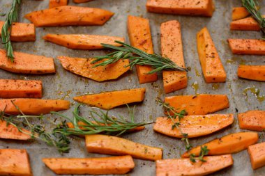 Yakın planda bir tepsi fırında patates cipsi. Kırmızı biber, biberiye ve tuzla pişirilmiş. Ev yapımı tatlı patatesler, baharatlar ve fırın tepsisinde bitkiler..