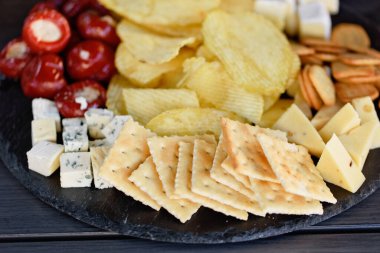 Farklı aperatifler ve aperatiflerin karışımı. Çeşitli atıştırmalıklarla dolu sokak yemekleri: Ekmek, baharatlı kraker, patates kızartması ve sos, domates, koyu arka planda lezzetli peynir. Antipasto tabağı