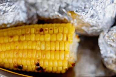 Folyoyla kaplanmış ızgarada pişirilmiş mısır koçanları. Ev yemeği. fırında mısır. Yaz pikniği, temiz havada dinlenme kavramı. Bahçede barbekü.