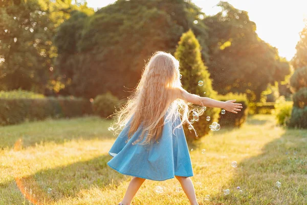 孩子们在草地上打滚跳舞玩泡泡的女孩美丽的金发小女孩在日落公园与肥皂泡共舞 — 图库照片