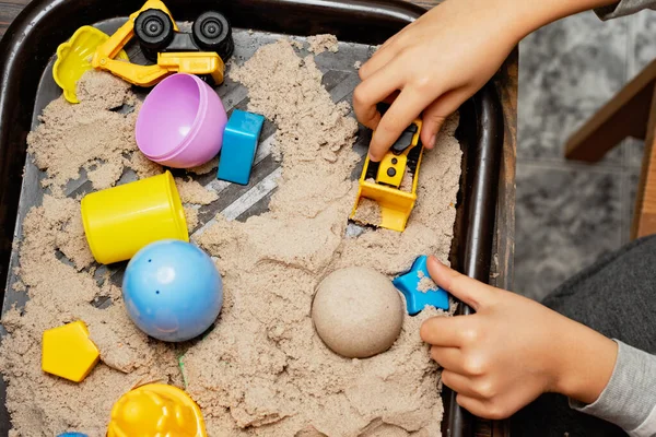 Child playing with kinetic sand and toy construction machinery. Hand of child in sand close up. Flat lay, top view. Indoor Table Game. Creativity Game concept. Activity for fine motor development