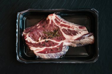 Koyu arkaplanda çiğ biftek ve baharat vakumu. Üst Manzara. Hava geçirmez ambalaj. Süpürgeyle paketlenmiş et