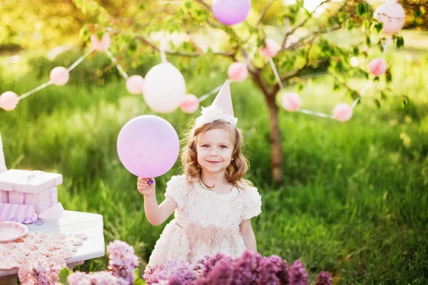 美しい庭のピンクの装飾とケーキの上に願いを吹くキャンドルを作る幸せな誕生日の女の子 4歳の誕生日 子供は幸せな誕生日ピンクのカップケーキを食べる カラフルなパステル装飾屋外 — ストック写真