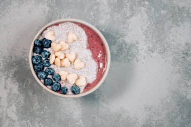 Üzerinde muz, granola, yabanmersini ve fotokopi alanı olan chia tohumları olan sağlıklı kahvaltı meyve suyu kasesi. Lezzetli yaban mersini suyu kasesi. Çiğ vejetaryen yemeği. Seçici odaklanma. Düz Yatay