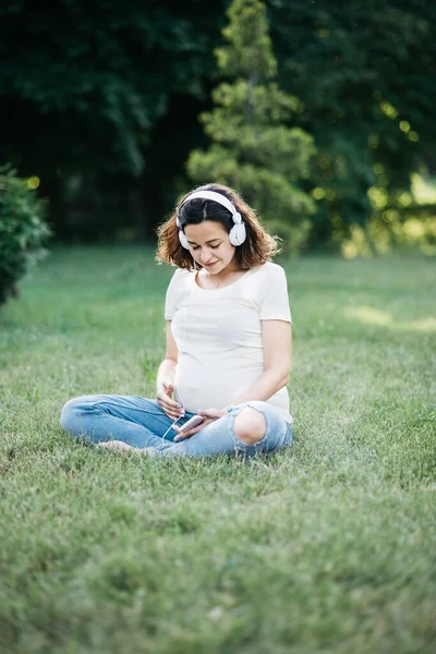 헤드폰끼고 임신중이에요 공원에서 스마트 폰으로 헤드폰으로 음악을 온라인 라디오 하우스 — 스톡 사진