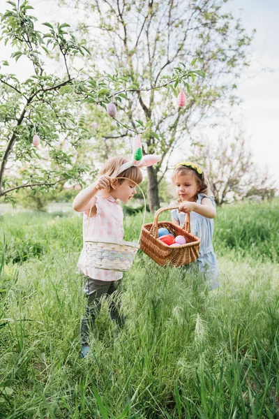 イースターエッグハント 庭でイースターエッグハントでカラフルな卵を拾うために実行しているバニー耳を身に着けている子供たちのグループ イースターの伝統 — ストック写真