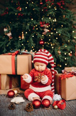 Noel ağacının altında küçük bir çocuk. Noel Baba şapkalı bebek. Noel ağacının altında hediyeler ve hediyeler. Mutlu tatiller, yeni yıl. Evde sıcak bir kış akşamı. Xmas zamanı.