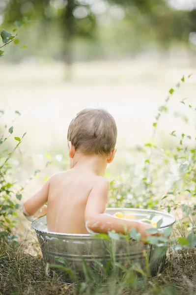 外にはゴム製のおもちゃの小さな男の子風呂があります 晴れた日 硬化だ 夏の庭で水の手順を取ってかわいい赤ちゃん 子供はお風呂で水遊び 健康で幸せな子供時代のコンセプト — ストック写真