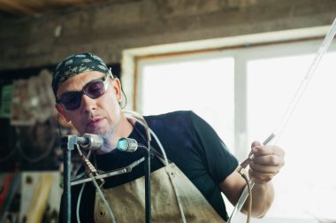 Alevlerle çalışan cam üfleyiciyi kapat. El yapımı, yüksek kalite, zanaatkar. Neon tüplerin üretimi. Gaz ocağı. El işi ve işçiliğin ayrıntıları. Patlamış erime