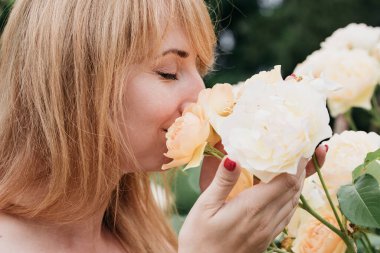 Bahar ve yaz. Genç bayan sevimli sarışın pembe çiçeğin kokusunu kokluyor. Parfüm ve kozmetik. Yaban güllerinin çiçeği. Gizli bahçe konsepti.
