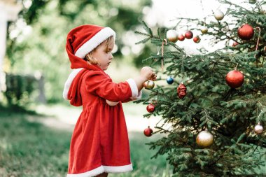 Temmuz 'da Noel. Çocuk temmuzda Noel 'i ağaçta bekliyor. Noel ağacı süsleyen küçük bir kızın portresi. Kış tatili ve insanların konsepti. Mutlu Noeller ve mutlu tatiller.