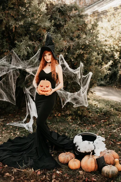 ハロウィン魔女は魔法の本で魔女を作る赤毛の女性彼女の手の中に魔法 魔女の帽子をかぶった美しい若い女性が現れます 不気味な暗い魔法の森の背景 魔術師 — ストック写真