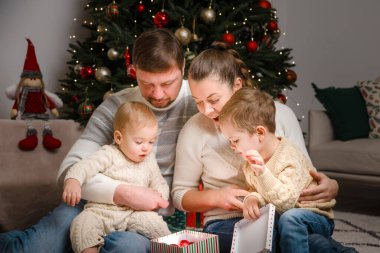 Neşeli bir aile anı. Ebeveynler ve iki küçük çocuk Noel hediye kutusunun etrafında toplandılar. mevsimsel, yaşam tarzı veya aile temalı içerik