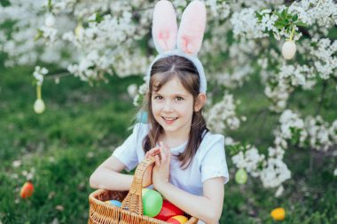 Paskalya yumurtası avında elinde paskalya sepeti tutan mutlu çocuk portresi. Neşeli açık hava aile anı Paskalya, çocukluk ve mevsimlik gelenekleri kutluyor..
