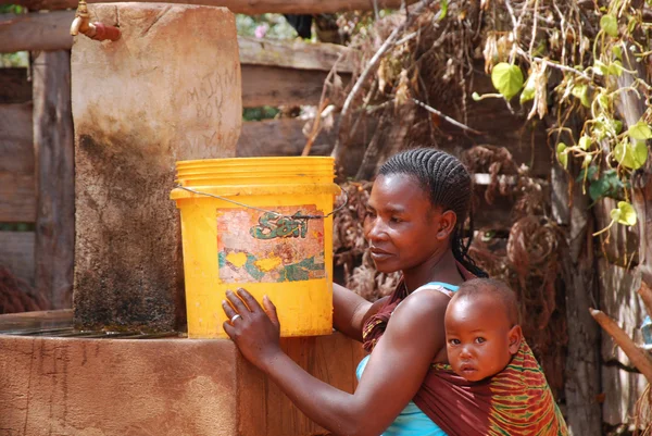 Una madre con su hijo en una fuente pública con un cubo de wa —  Fotos de Stock
