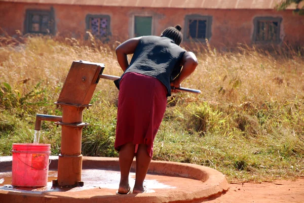 En kvinna och pumpa vatten från en offentlig fontän-Pomerini-Tanzania- — Stockfoto