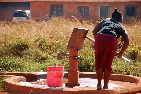 Una donna e pompa acqua da una fontana pubblica-Pomerini-Tanzania - — Foto Stock