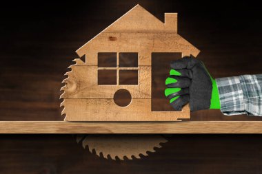 Marangoz koruyucu iş eldivenleriyle ahşap model ev şeklinde elektrikli testere kullanıyor..