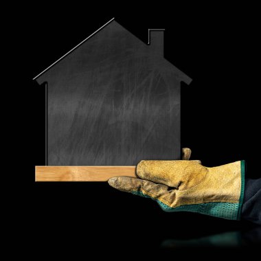 Koruyucu iş eldivenli bir el, küçük bir ev şeklinde boş bir karatahta gösteriyor. Siyah arka planda, kopyalama alanı olan izole edilmiş..