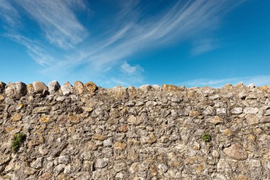 Taşlardan ve betondan yapılmış, mavi gökyüzü ve arka planda bulutlarla kaplı bir sınır duvarı. Verona ili, Veneto, İtalya, Avrupa.