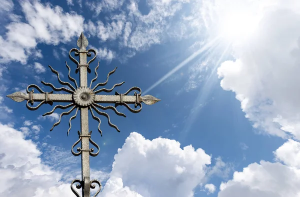 Closeup of a wrought iron religious cross on beautiful blue sky with clouds and sun rays. Veneto, Italy, Europe