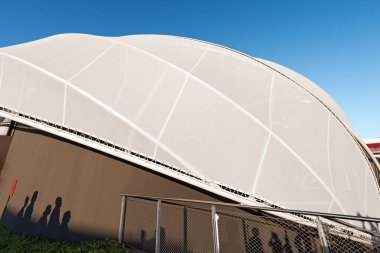 Temiz mavi gökyüzü üzerinde modern bir gerilme yapısına yakın çekim, beyaz çelik direkli çadır bezi çatısı. Fotoğraf, tam çerçeve.