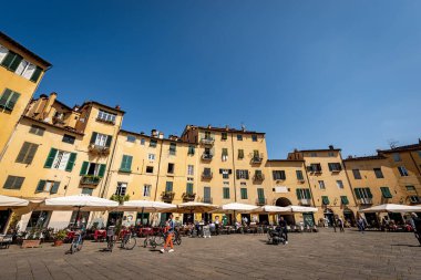 LUCCA, İtalya - 16 Nisan 2017: Lucca şehir merkezindeki Piazza dell 'Anfiteatro (Amfitiyatro Meydanı). Turistler ve yerliler antik eliptik şehir meydanını ziyaret ediyorlar. Toskana, İtalya, Avrupa.