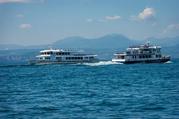 Two ferry boats in motion in front of the small village of Bardolino on Lake Garda (Lago di Garda), Verona province, Veneto, Italy, Europe. On the horizon the coast of Lombardy with the mountains.