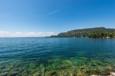 Garda Gölü kıyısındaki küçük Garda kasabasının önündeki sahil şeridi (Lago di Garda). San Vigilio Burnu (Punta San Vigilio) ile güzel bir körfez. Verona, Veneto, İtalya, Avrupa