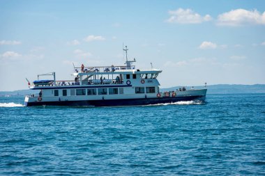 Garda Gölü (Lago di Garda), Verona ili, Veneto, İtalya, Avrupa 'daki Bardolino köyünün önünde seyir halinde bulunan feribot. Ufukta tepeli Lombardy sahilleri.