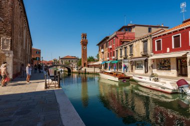 MURANO, ITALY - 2 Haziran 2021: Murano adası şehir merkezi, küçük bir kanalı, tekneleri, evleri ve dükkanları olan antik Civic Tower veya Saat Kulesi. Venedik, Veneto, İtalya, Avrupa