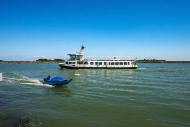 Venedik, İtalya - 2 Haziran 2021: feribot ve Venedik 'te Torcello ve Burano adasının önündeki gölde hareket halindeki küçük bir motorlu tekne. Venedik, UNESCO dünya mirası sahası, Veneto, İtalya, Avrupa.