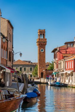 MURANO, ITALY - 2 Haziran 2021: Murano adası şehir merkezi, küçük bir kanalı, tekneleri, evleri ve dükkanları olan antik Civic Tower veya Saat Kulesi. Venedik, Veneto, İtalya, Avrupa.