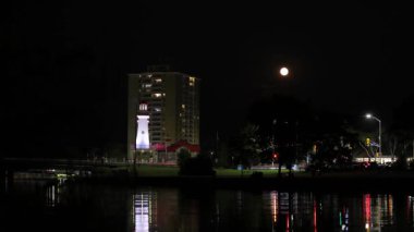 Dolunay deniz fenerinin zaman atlamasında yükseliyor. Nehir ışığı yansıtıyor, arabalar köprüden geçiyor, gece hayatı, Port Credit 'in tarihi bir bölümü, Mississauga, Ontario, Kanada