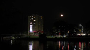 Dolunay gökyüzünde canlı bir şehrin arka planında yükseliyor, trafik yolda, deniz fenerinde çalışıyor, nehirde sakin dalgalar - Mississauga, Ontario, Kanada 'nın gece hayatı