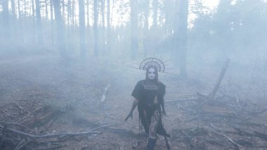 Cadı suretinde genç bir kadın karanlık ve sisli ormanda siyah elbiseli ve kafasında taçla yürüyor..