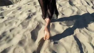 Siyah şeffaf elbiseli güzel bir kadın kum ocağında yalınayak yürüyor ve suya bakıyor..