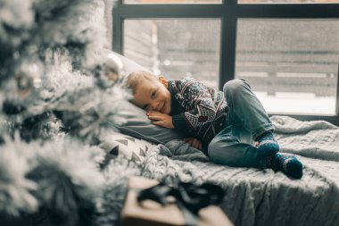 Mutlu çocuk, Noel ağacının yanındaki pencere eşiğinde süslemelerle yatıyor..