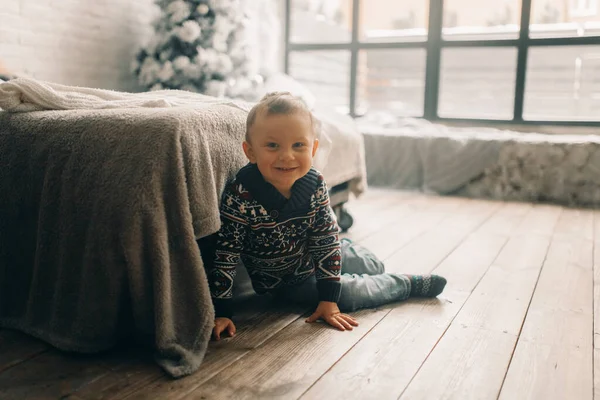 幸せな子供の男の子はクリスマスツリーと窓に対してベッドの近くの床に座っています — ストック写真