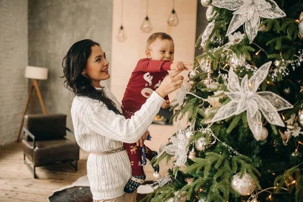 幸せな母親とともに彼女の息子はクリスマスツリーの近くのクリスマスの装飾を見て — ストック写真