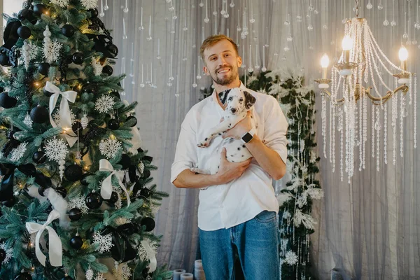 Jongeman Staat Buurt Van Kerstboom Met Decoraties Speelt Met Pup — Stockfoto