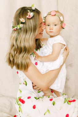 Genç anne gülümser ve küçük kızını kafasında çelenkle tutar..