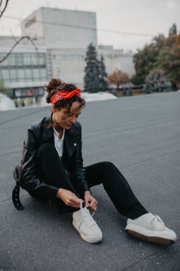 Güzel genç bir kadın şehrin kaldırımlarında oturuyor ve spor ayakkabılarına ayakkabı bağları takıyor..