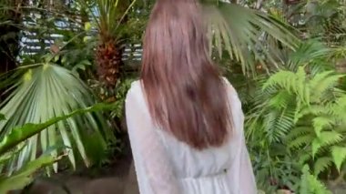 Genç bir kadın, yeşil tropikal bitkiler arasında portakalların içinde beyaz elbiseler içinde yürüyor..