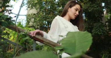 Beyaz elbiseli genç kadın, yeşil tropikal bitkilerin arka planına karşı portakalların içinde merdivenlerden aşağı iniyor..