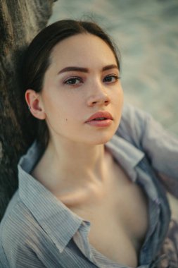 Plajda, ağaç gövdesinin yanında genç bir kadının portresi. Üst görünüm.