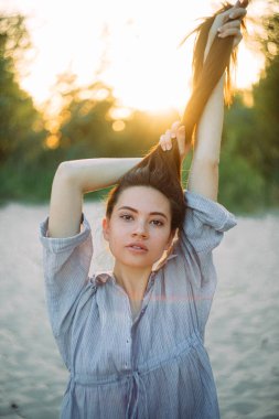 Genç bir kadın kumsalda poz verir ve gün batımında saçını kaldırır..