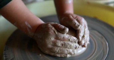 Çocuk elleri, atölyede dönen çömlek çarkı üzerinde çalışan toprak kaplarını yontuyor..